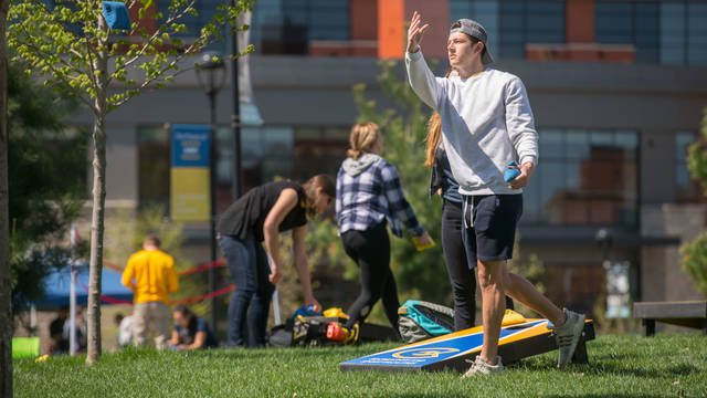 Male student tossing bags for bean bag game on campus mall, spring