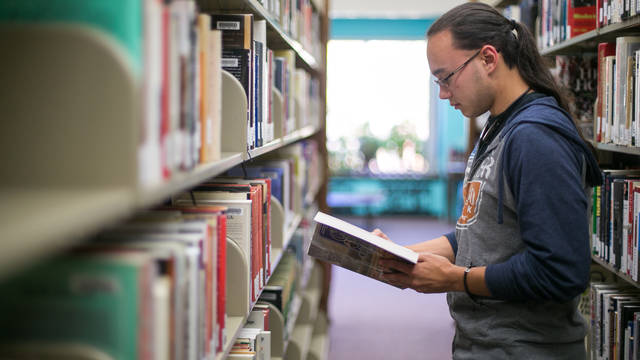 Male student in the library stacks looking at a book