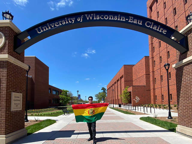 Alejandro Lama in the campus archway holding Bolivian flag.
