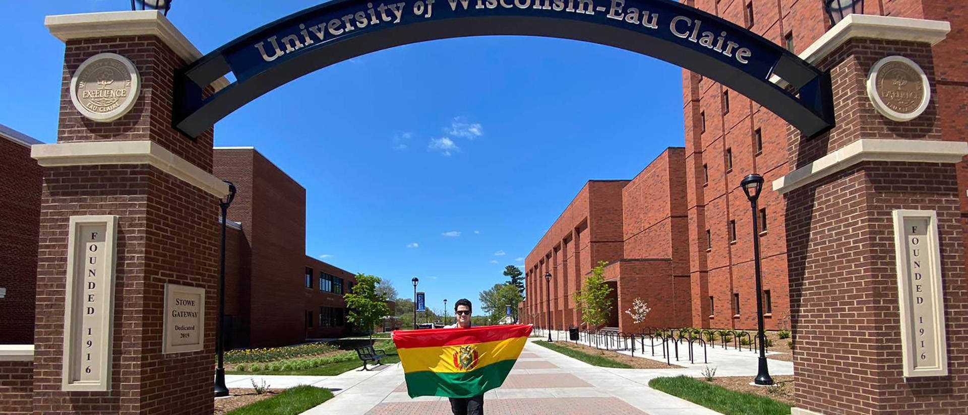 Alejandro Lama in the campus archway holding Bolivian flag.