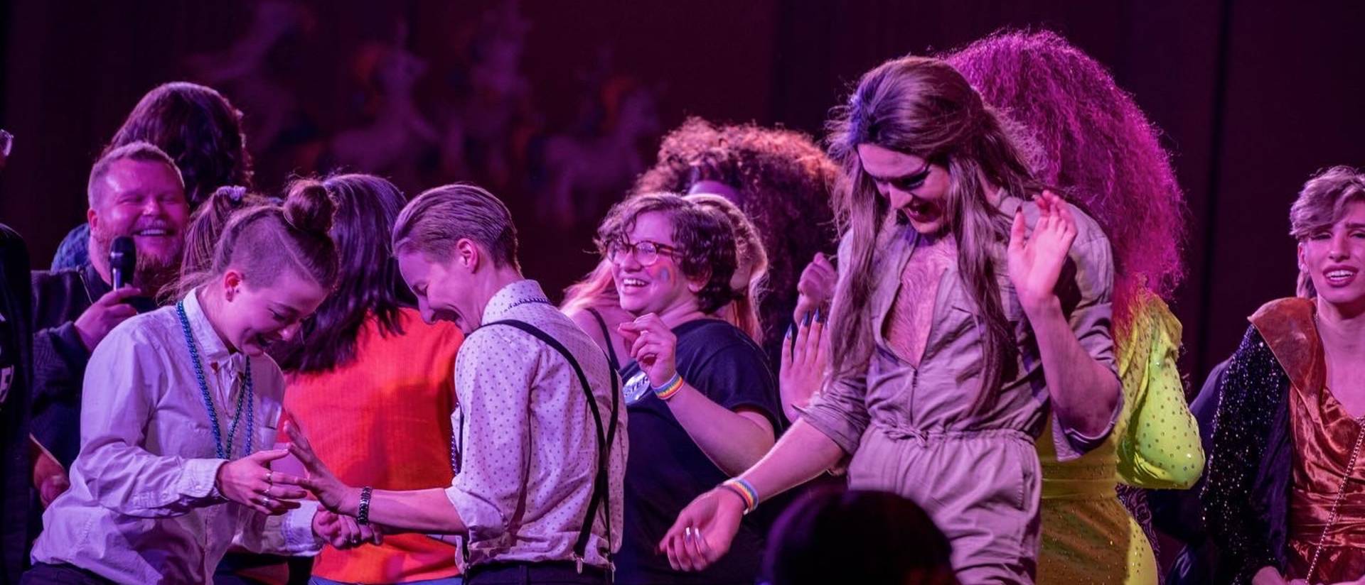 Close-up of LGBTQ+ students dancing and smiling on a large stage.