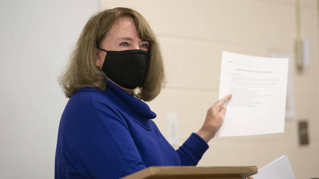 Instructor in mask holding up a paper while addressing class