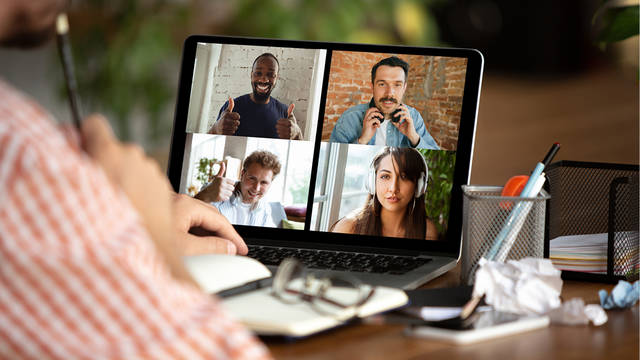 Student sitting at a table participating in an online meeting with 4 individuals displayed on his computer