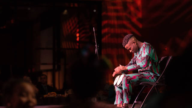 Olu Famule drumming on a stage in Nigerian traditional clothing