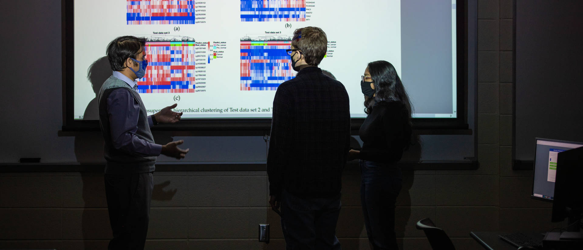 Computer science students standing in front of a projected image discussing