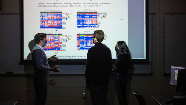 Computer science students standing in front of a projected image discussing
