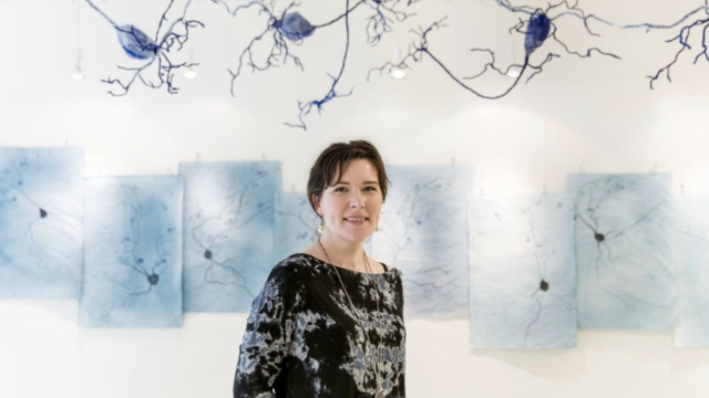 Kindra Crick stands smiling in front of your artwork