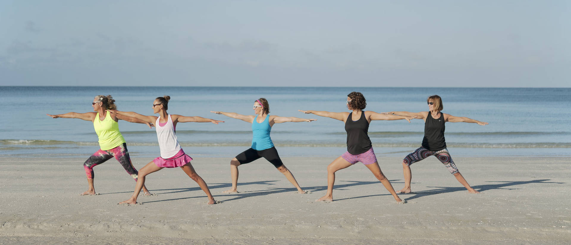 Image of people practicing yoga on beach in summer.