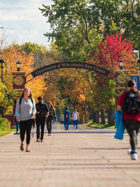 学生走在秋叶之间的人行道上，背景是威斯康星大学欧克莱尔拱门。