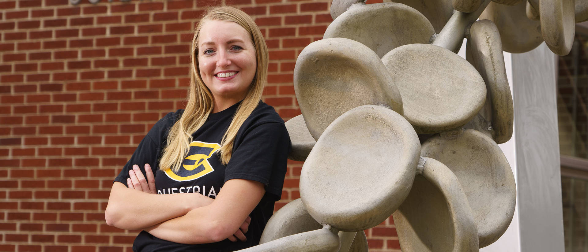 Female student leaning on sculpture outside science building