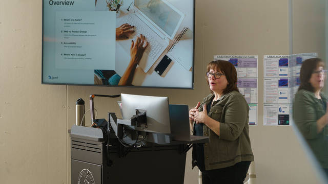 Woman in a classroom showing a Powerpoint on a screen.