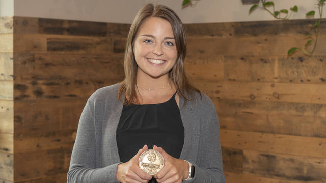 Megan Baier smiles happily holding a university medallion
