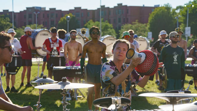 Drum and bugle corps practicing outside, girl holding up a drum