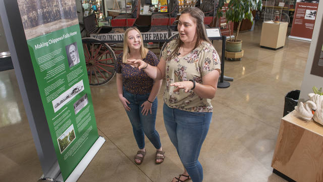 UW-Eau Claire public history graduate students Jordan Stish (left) and Alexi Linder discuss the exhibit they helped create in the Irvine Park Welcome Center in Chippewa Falls. (Photo by Shane Opatz)