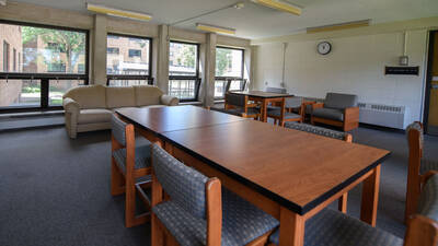 A common space in Sutherland Hall with multiple windows, a couch and many tables and chairs