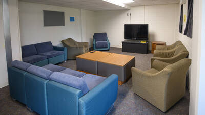 A common area featuring two couches and multiple armchairs surrounding a television
