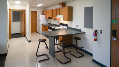 Kitchen area in a Chancellors Hall appartment with fridge, dishwasher, sink, oven, and counter with stools.