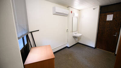 Alternate view of single room in residence hall with a sink, mirror and door to unit