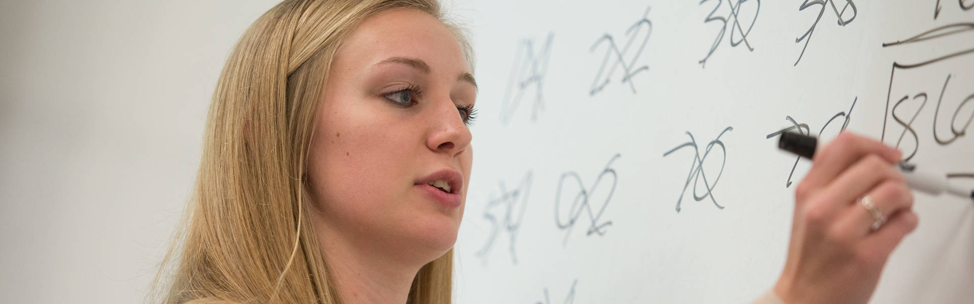 Female student at the white board doing math. 